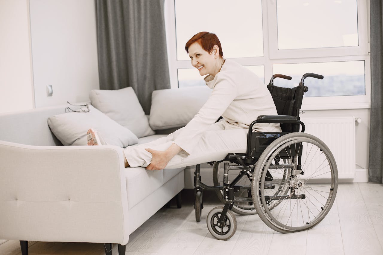 Smiling woman in wheelchair stretches legs on sofa in bright modern living room.